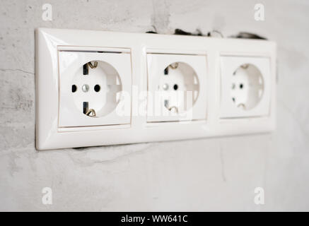 Elektrische EU-Steckdose auf grauem Beton Wand Hintergrund. Reparatur in einer Wohnung oder im Büro, Austausch von elektrischen Leitungen. Nahaufnahme. Stockfoto