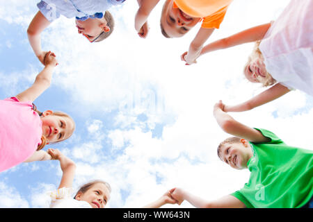 Ansicht von unten Kinder gemeinsam im Kreis halten sich an den Händen fest und stehend, ihre Zusammengehörigkeit zu zeigen. Mitschüler in einem Summer Camp teamb spielen Stockfoto