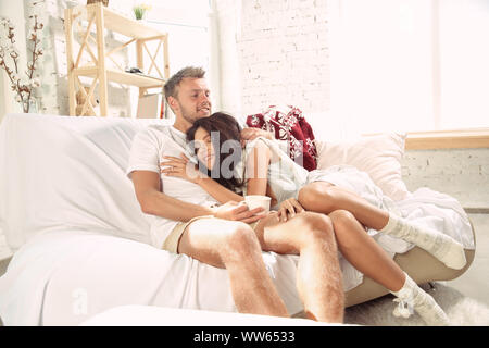 Paar Liebhaber zu Hause entspannende zusammen. Kaukasische Mann und Frau Wochenende in, Sieht Ausschreibung und glücklich. Konzept der Beziehungen, Familie, Herbst und Winter Komfort. Tee trinken und sich umarmen. Stockfoto