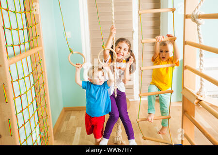 Drei aktive Kinder in bunten T-Shirts, zusammen excercising, Hängen und Klettern auf einem Seil, Leiter und Ringe auf Ihre kommen Sport Komplex. Aktiv Stockfoto