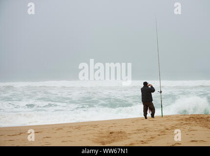 Mann mit Angel am Strand, Meer, Wellen, Schaum, Wind Surf Stockfoto