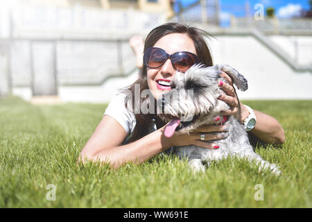 Ziemlich erwachsenen kaukasischen glückliche Frau im Park Ruhe an einem sonnigen Tag mit ihrem geliebten Hund. Weibliche lag auf dem Gras lächelnd und mit Blick auf die Kamera Stockfoto