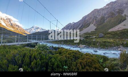 Hängebrücke über den Fluss mit schneebedeckten Bergen im Hintergrund auf der Hooker Valley Track, Neuseeland Stockfoto