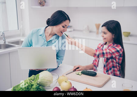 Porträt von zwei schön süß Schöne attraktive Süß heiter fröhlichen Leute Mädchen Fütterung Mom frische Gurke in hellen weißen Küche Innenbereich Im Innenbereich Stockfoto