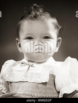 1950er Jahre lockiges Haar Baby Mädchen trägt ein Kleid mit SMOCKING SCRUNCHING BIS GESICHT SCHMOLLEND AUF KAMERA-b 1468 HAR 001 HARS SCHMOLLEND STIMMUNG MISSBILLIGUNG HIMBEERE SCRUNCHING Wachstum von Jungfischen SAUER HALTUNG BABY GIRL SCHWARZ UND WEISS KAUKASISCHEN ETHNIE lockiges Haar ABNEIGUNG HAR 001 ALTMODISCH SMOCKING Stockfoto