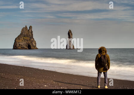 Touristische auf seinem Rücken in Anorak mit Kapuze die Drei Schwestern Betrachtung in Vik am Strand Stockfoto