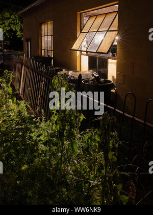 Fenster mit Licht, Müll, Mülltonnen, die bei Nacht Stockfoto