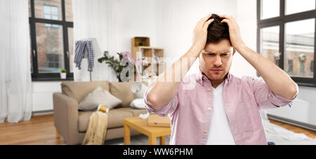 Verzweifelten jungen Mann in unordentlichen Zimmer in Kopfschmerzen Stockfoto