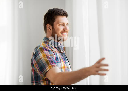 Junger Mann öffnen Fenster Vorhang zu Hause Stockfoto