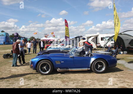 Besucher bei einer Veranstaltung auf einer AC Cobra angloamerikanischen Kit Car und andere Fahrzeuge suchen auf Anzeige an Kent, UK. Sommer 2019. Stockfoto