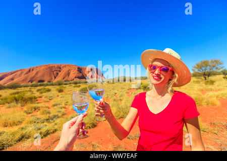 Frau cheers Tun am Uluru Ayers Rock bei Sonnenuntergang im Uluru-Kata Tjuta National Park zu feiern. Blond Reisenden im australischen Outback Red Centre Stockfoto