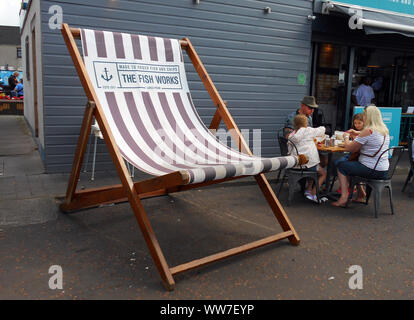 Eine extra große Liegestuhl neben dem Fisch und Chip Shop sitzt, dass es Werbung, an der Küste der Sea Side Stadt Largs im Firth of Clyde, Schottland. Kunden gesehen zu verstauen, in der Nähe dieser riesigen Stuhl! Alan Wylie/ALAMY © Stockfoto