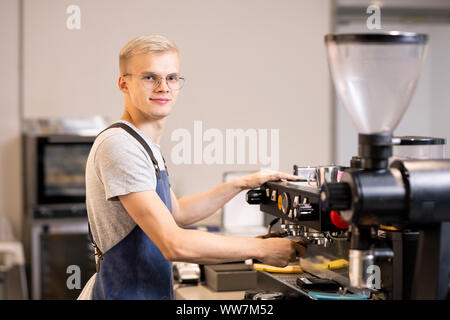 Erfolgreiche barista in Uniform mit Kaffeemaschine im Stehen durch Arbeitsplatz Stockfoto