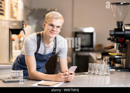 Gerne Kellner mit Stift und Smartphone stehen am Arbeitsplatz vor der Kamera Stockfoto