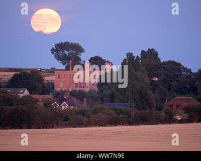 Eastchurch, Kent, Großbritannien. 13. September, 2019. UK Wetter: Die vollständige Harvest Moon gesehen steigende über historische Shurland Halle (wo Henry VIII seine Flitterwochen verbracht) in Eastchurch, Kent an diesem Abend. Hinweis: Ein Traktor kann gesehen werden Ernte unter dem Mond links von shurland Halle. Credit: James Bell/Alamy leben Nachrichten Stockfoto