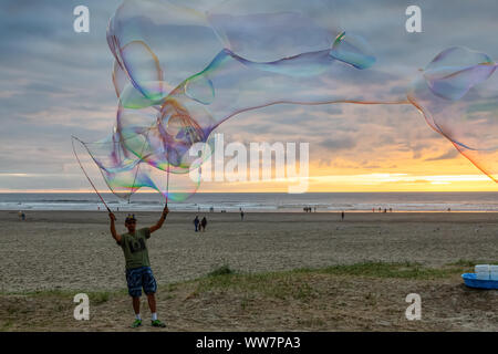 Seaside, Oregon, USA - September 6, 2019: Der Mensch, der grosse Seifenblasen am Sandstrand in einer dramatischen Sommer Sonnenuntergang. Stockfoto