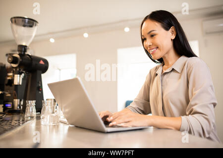 Junge glücklich weibliche Unternehmer durch Arbeitsplatz vor Laptop Stockfoto