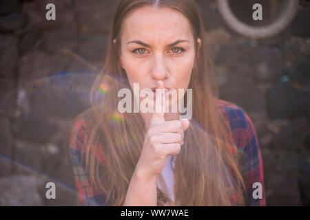 Portrait von Angry kaukasischen junge Frau mit Finger am Mund stille Mann zu sagen. starke und unabhängige Frau mit blauen Augen. sun Flair auf dem Bild Stockfoto