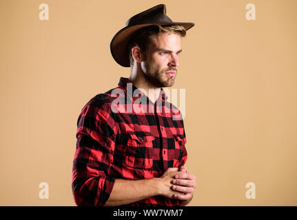 American Cowboy. Westliche leben. Mann unrasiert Cowboy beigen Hintergrund. Unrasierten Kerl in Cowboyhut. Schöne bärtige Macho. Schönheit Standard. Beispiel wahrer Männlichkeit. Cowboy Hut tragen. Stockfoto