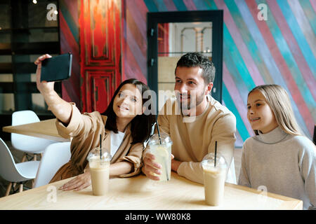 Junge fröhliche Familie von drei Ruhen von Tisch im Cafe nach dem Einkaufen Stockfoto