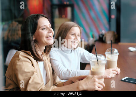 Ekstatisch Weiblichen und ihre hübsche Tochter mit Milch Cocktails im Café lachen Stockfoto