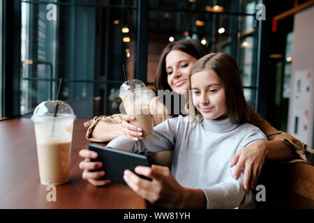 Glückliche Mutter, die ihre Tochter mit Smartphone während beide Videos ansehen Stockfoto