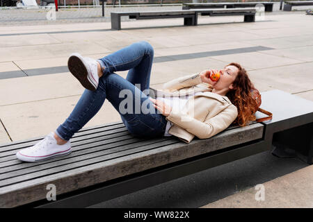 Junge Frau liegt auf einer Bank und in einen Apfel beissen Stockfoto