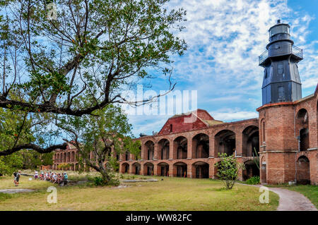 Eine Gruppe von Menschen sitzen in Hof, Beginn einer Tour von Fort Jefferson, mit Baum und Leuchtturm gegen Wände aus Backstein. Dry Tortugas National Park. Stockfoto