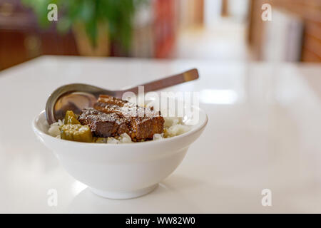 Nahaufnahme des Lu Rou Ventilator, Taiwanesische langsam kochen Sojasauce geschmorten Schweinebauch, mit Reis in der kleinen weißen Schale und weißer Tisch. Stockfoto