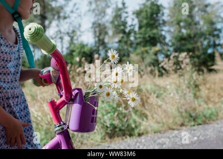 Kleine Mädchen Fahrrad mit wilden gepflückten Blumen im Korb Stockfoto