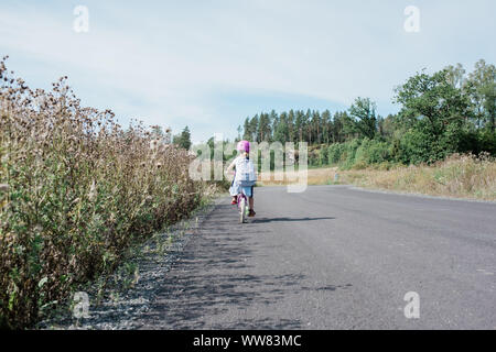 Rückansicht eines jungen Mädchens Radfahren nach Hause von der Schule entlang der Landstraße Stockfoto