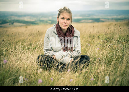 Junge Frau sitzt im Gras Wiese auf Kamera, Revel, Tarn, Frankreich Stockfoto