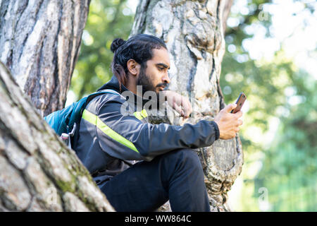 Junge Wanderer Indien sitzen und Kontrolle smart phone Stockfoto