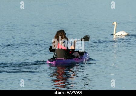 Eine weibliche Kayaker gemächlich Paddel, up Paddle Boarding, paddleboarding, Paddel boarder Surfen auf die marine Lake auf der Promenade in Southport, Großbritannien Stand Stockfoto