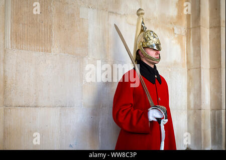 LONDON - 31. Oktober 2016: Eine junge Königin Life Guard in voller Uniform mit Royal Red Coat und goldenen Helm steht an Aufmerksamkeit mit einem Schwert. Stockfoto