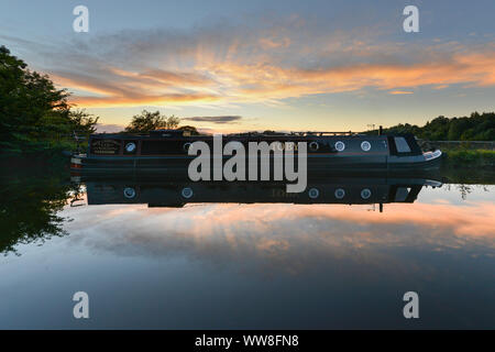 Reflektion von einem schmalen Boot auf einen ruhigen Abend mit einem Sonnenuntergang auf dem Leeds & Liverpool canal Stockfoto