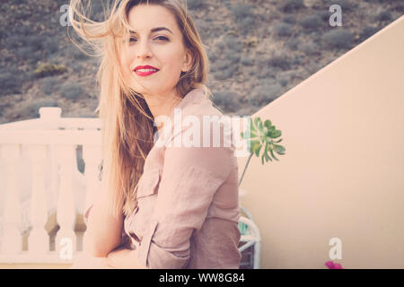 Portrait von lächelnden Mädchen mit roten Lippenstift und langen blonden Haar weht im Wind, Schönheit und Jugend Konzept Aufenthalt im Freien auf der Terrasse mit der Natur Berge im Hintergrund, sonnigen Tag des Sommers Stockfoto