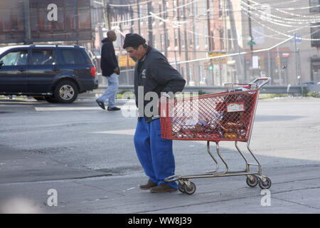 Alten Mann, der einen Supermarkt Warenkorb mit leeren Getränkeverpackungen auf den Straßen von Philadelphia, PA, USA Stockfoto