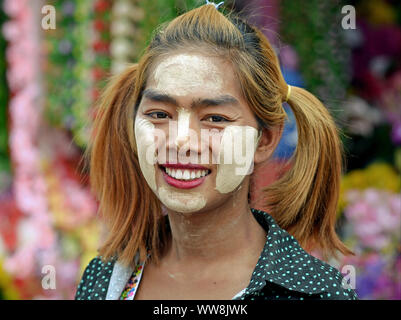 Die jungen burmesischen Frau mit langen Zöpfen und starken Flecken der gelblich-weißes, traditionelles thanaka Gesicht Kosmetik alle über ihr Gesicht ein Lächeln für die Kamera. Stockfoto