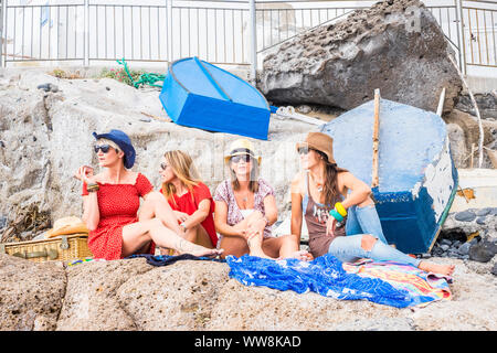 Gruppe von Frauen Freunde sitzen auf den Felsen in der Nähe des Meeres und genießen Sie Urlaub und Freizeit Outdoor Aktivität Entspannung in Freundschaft. glücklich Lifestyle Menschen, vier Frauen, die zusammen unter der Sommersonne Aufenthalt Stockfoto