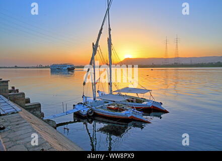 Segelboote, FELUCCAS am Ufer des Nils mit River Cruise Schiff bei Sonnenuntergang, Karnak in der Nähe von Luxor, Oberägypten, Ägypten Stockfoto