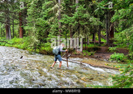 Man überquert den Fluss starke aktuelle Ford auf Rätsel Creek Trail in Aspen, Colorado im Jahr 2019 Sommer im Wald Holz Stockfoto