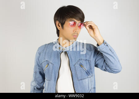 Jungen asiatischen Mann in Jeans Jacke oder Jeansjacke Touch Red Gläser und Unten. Denim oder Jeans Jacket Men Fashion auf grauem Hintergrund Stockfoto