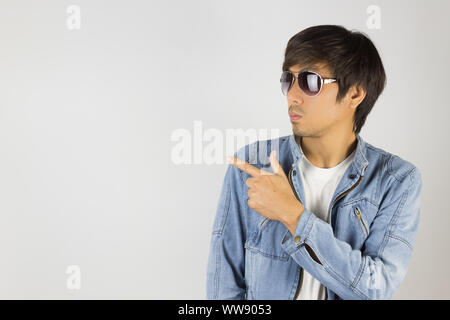 Jungen asiatischen Mann in Jeans Jacke oder Denim Jacke tragen Sie eine Sonnenbrille und Zeigefinger. Denim oder Jeans Jacket Men Fashion auf grauem Hintergrund Stockfoto