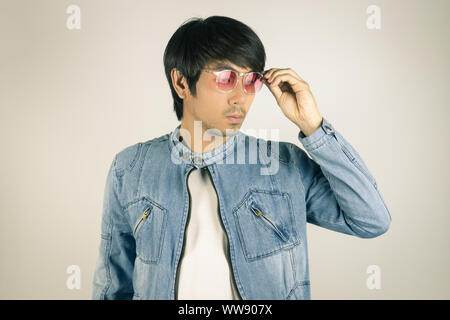 Jungen asiatischen Mann in Jeans Jacke oder Jeansjacke Berühren rote Brille. Denim oder Jeans Jacket Men Fashion auf grauem Hintergrund Stockfoto