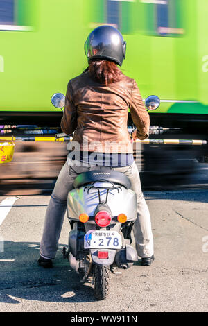 Person auf dem Motorrad mit vorbeifahrenden Zug im Hintergrund am Bahnübergang Stockfoto