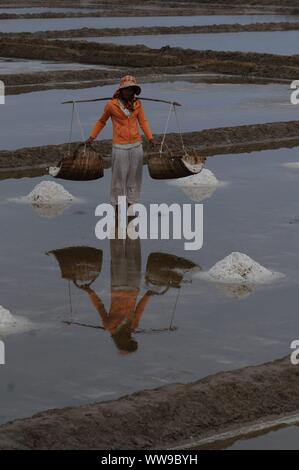 Reflexion eines Salzes Arbeiter tragen Rattankörbe beladen w/geerntete Salz in die Salzfelder, Kampot Province, Kambodscha. © kraig Lieb Stockfoto
