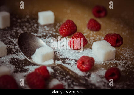 Beeren der roten Himbeeren mit einem Teelöffel und Würfel von raffiniertem Zucker liegen auf einem Holz- rustikalen Tisch Ansicht von oben. Stockfoto