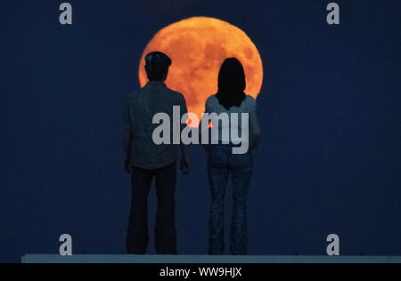 Eine Ernte Vollmond, der kurz vor der Herbsttagundnachtgleiche, signalisiert den Start in eine neue Saison auftritt, steigt an der Skulptur des 'Paar' des Künstlers Sean Henry in Newbiggin-by-the-Sea in Northumberland. Stockfoto