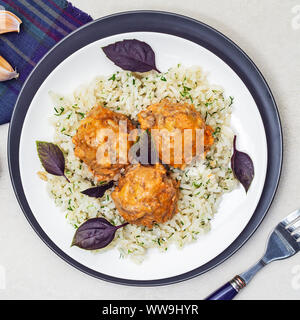 Frikadellen und Reis in einer weißen und schwarzen Platten mit Kräutern und Basilikum. Ansicht von oben Stockfoto